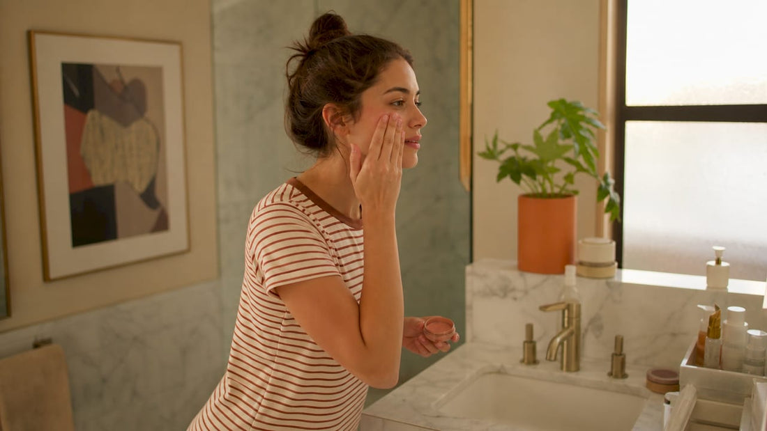 Young woman applying cream blush at vanity
