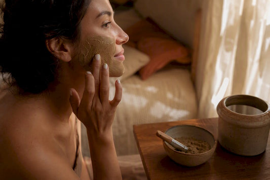 Hands applying clay mask on cheek