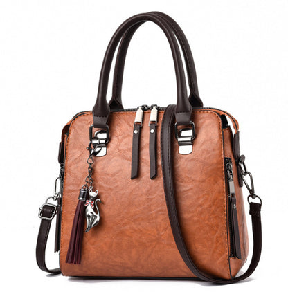 Brown leather handbag with dark handles, silver fox charm, and side zippers