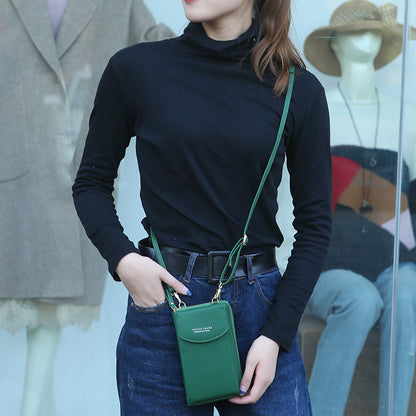Woman in black turtleneck and jeans with green crossbody phone bag standing by store window