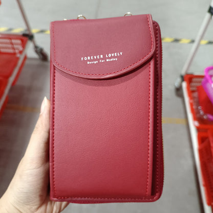 Hand holding red faux leather crossbody phone bag with 'Forever Lovely' text in a store