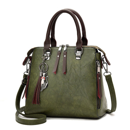 Olive green leather handbag with brown handles, shoulder strap, and cat tassel charm
