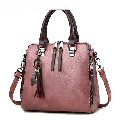 Pink leather handbag with top handles, detachable strap, tassel, and cat keychain charm