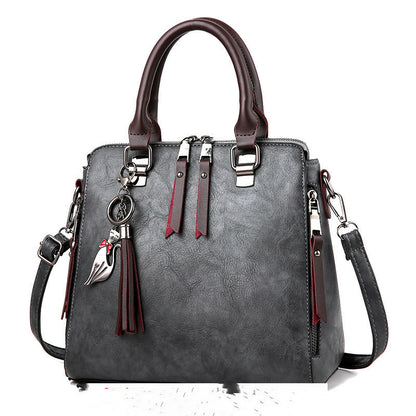 Elegant gray leather handbag with double handles, tassel keychain, and detachable strap