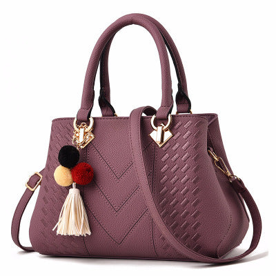 Purple leather handbag with textured pattern, gold hardware, pom-pom and tassel keychain