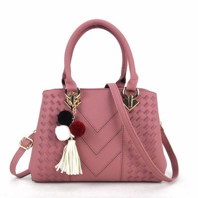Pink leather handbag with textured pattern, gold hardware, and pom pom tassel charm