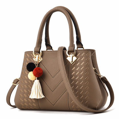 Taupe leather handbag with woven accents, top handles, shoulder strap, and pom pom tassel charm