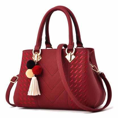 Red leather handbag with textured pattern, gold hardware, pompom tassel charm, shoulder strap