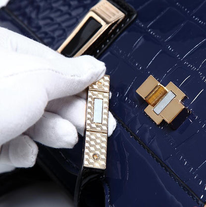 White-gloved hand opening gold clasp on navy blue crocodile embossed handbag