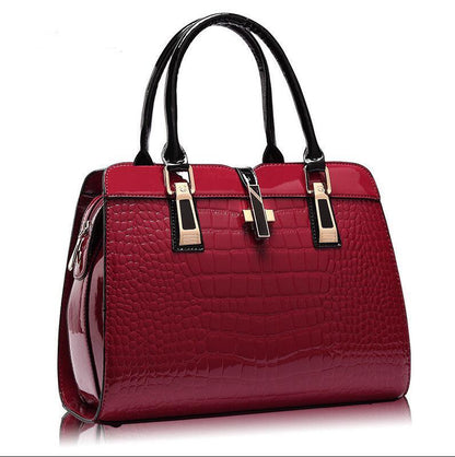 Glossy red crocodile pattern handbag with black handles and gold hardware on white background