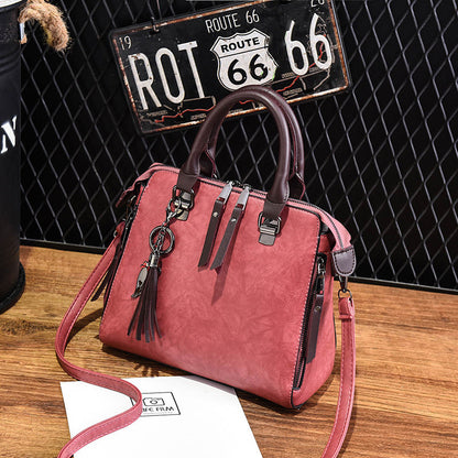 Pink leather handbag with tassel keychain, brown handles, on wooden table, Route 66 sign background