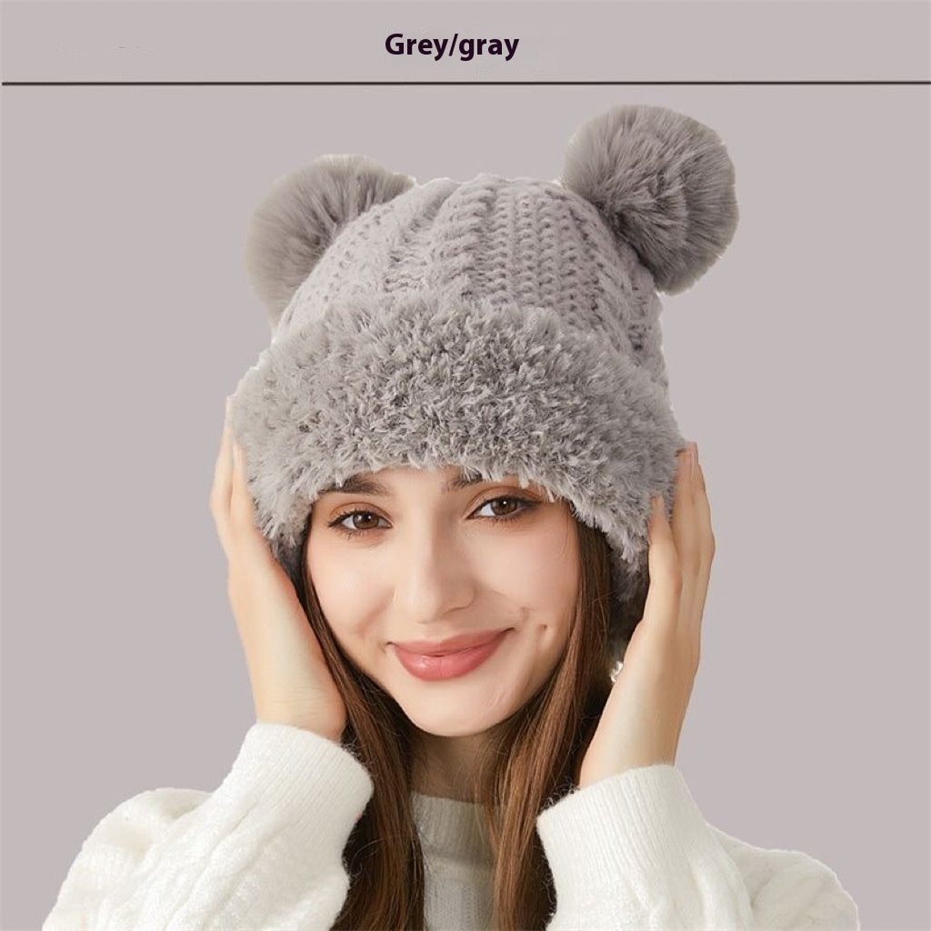 Woman wearing a grey knit winter hat with faux fur trim and pom-poms, cozy fashion accessory