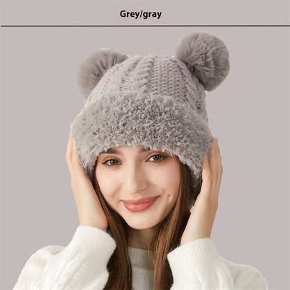 Woman wearing a grey knit winter beanie with faux fur trim and pom-poms, cozy fashion hat