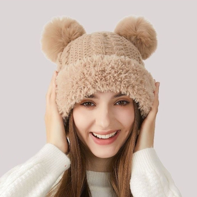 Woman smiling in a beige knit winter hat with faux fur and double pom poms