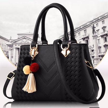 Elegant black leather handbag with gold hardware, tassel charm, and textured chevron pattern