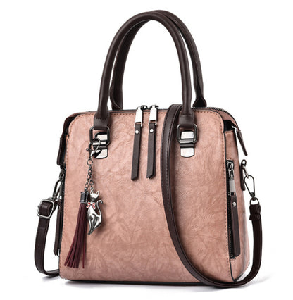 Pink leather handbag with brown handles, fox keychain, tassel, and shoulder strap